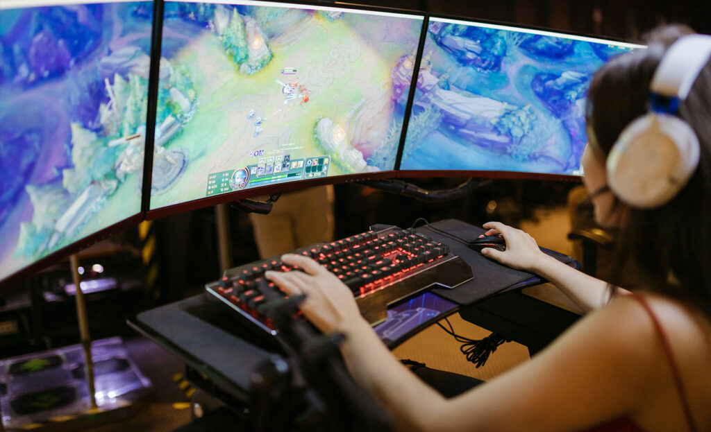 Frau spielt vor drei Monitoren Computer Games