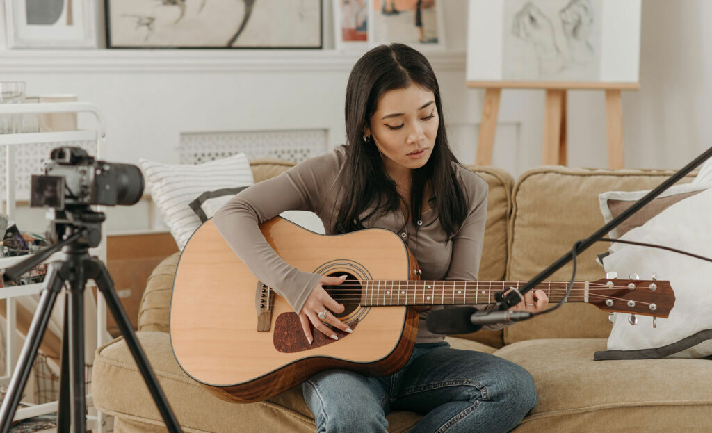 Frau mit Gitarre auf dem Sofa vor einer Kamera
